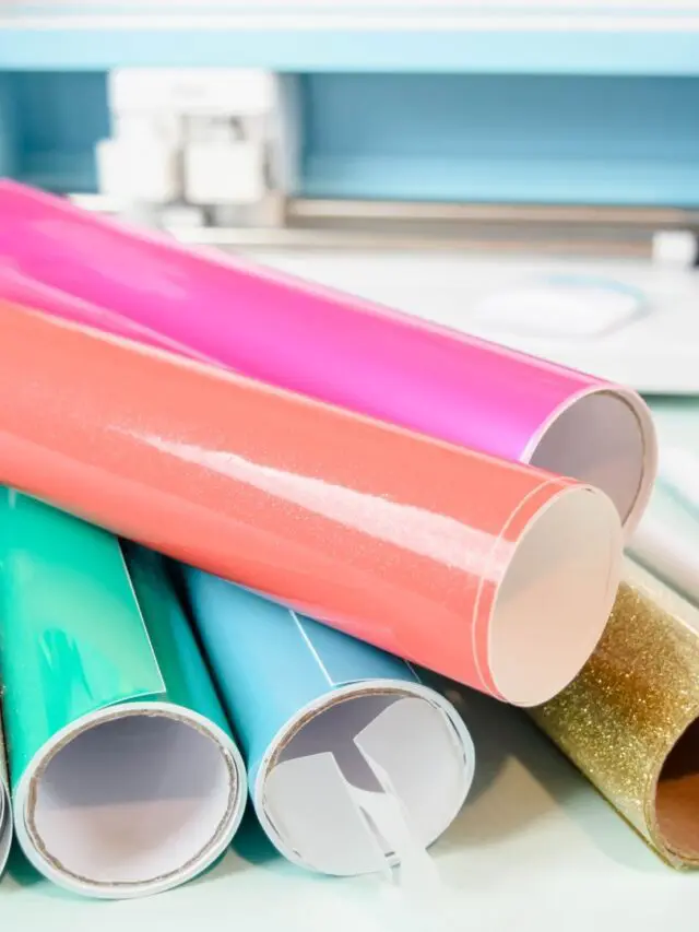 Colorful rolls of craft vinyl on a desk with a Cricut in the background