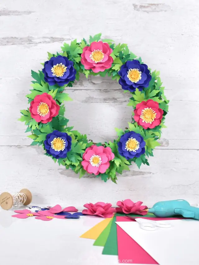 The image shows a pink, purple and green spring wreath. Looking for a fun, creative way to spruce up your front door this spring? Learn how you can make a beautiful paper flower primrose wreath with the help of our simple DIY tutorial and your Cricut machine!