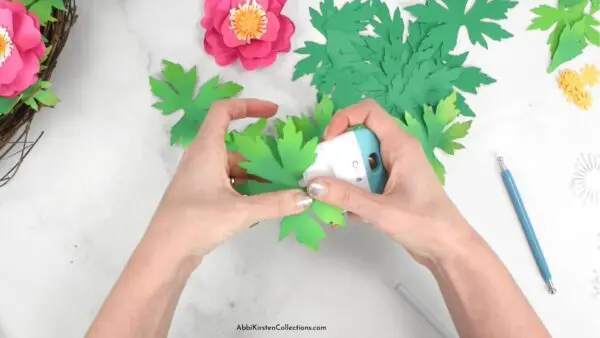 The image shows how to curl paper leaves with the Cricut scraper tool.