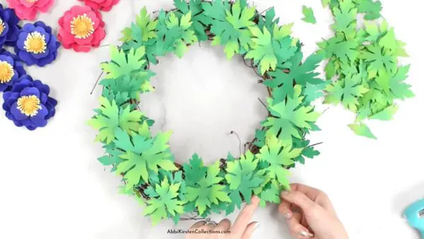 The image shows how to add paper leaves to a grapevine wreath base.