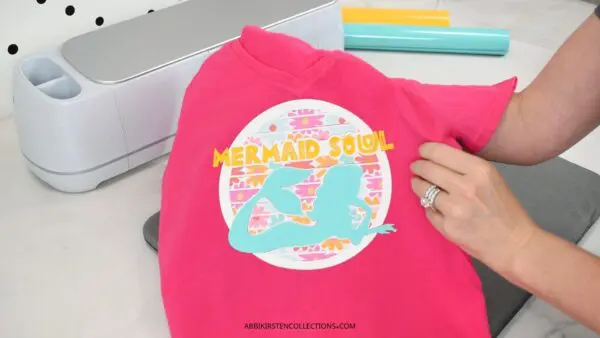 The image shows a pink t-shirt with a heat transfer vinyl design layered on using patterned vinyl. The shirt reads, Mermaid Soul with a mermaid and floral background.