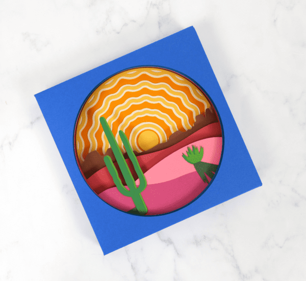 Layered shadow box paper craft made with Cricut. The scene is of a sunrise in the desert. 