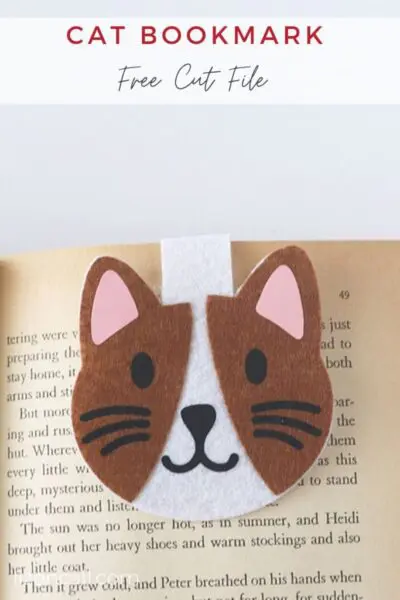 Felt brown and white cat face with pink ears and bookmark over book.