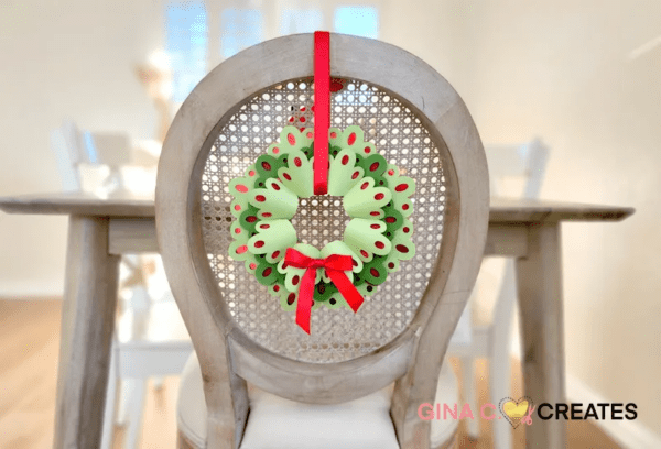 Layered paper Christmas wreath in shades of green with red ribbon hanging from back of chair