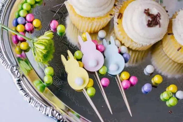 Three pastel bunny cupcake toppers on a silver tray with cupcakes.