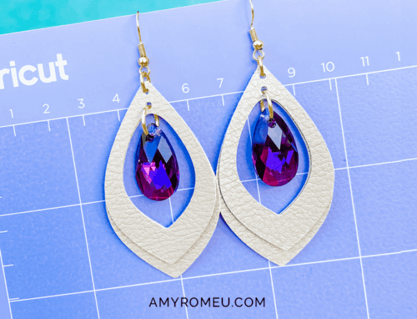 White faux leather earrings with pink crystals on a Cricut sheet.