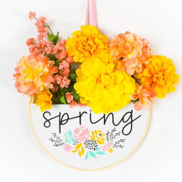 Embroidery hoop wreath with yellow and peach flowers with a SVG cut file that reads Spring added to the front with iron-on vinyl.