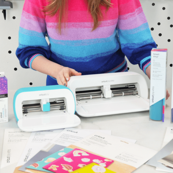 Women in bright colorful sweater and the Cricut Joy and Joy Xtra machines on a craft desk.