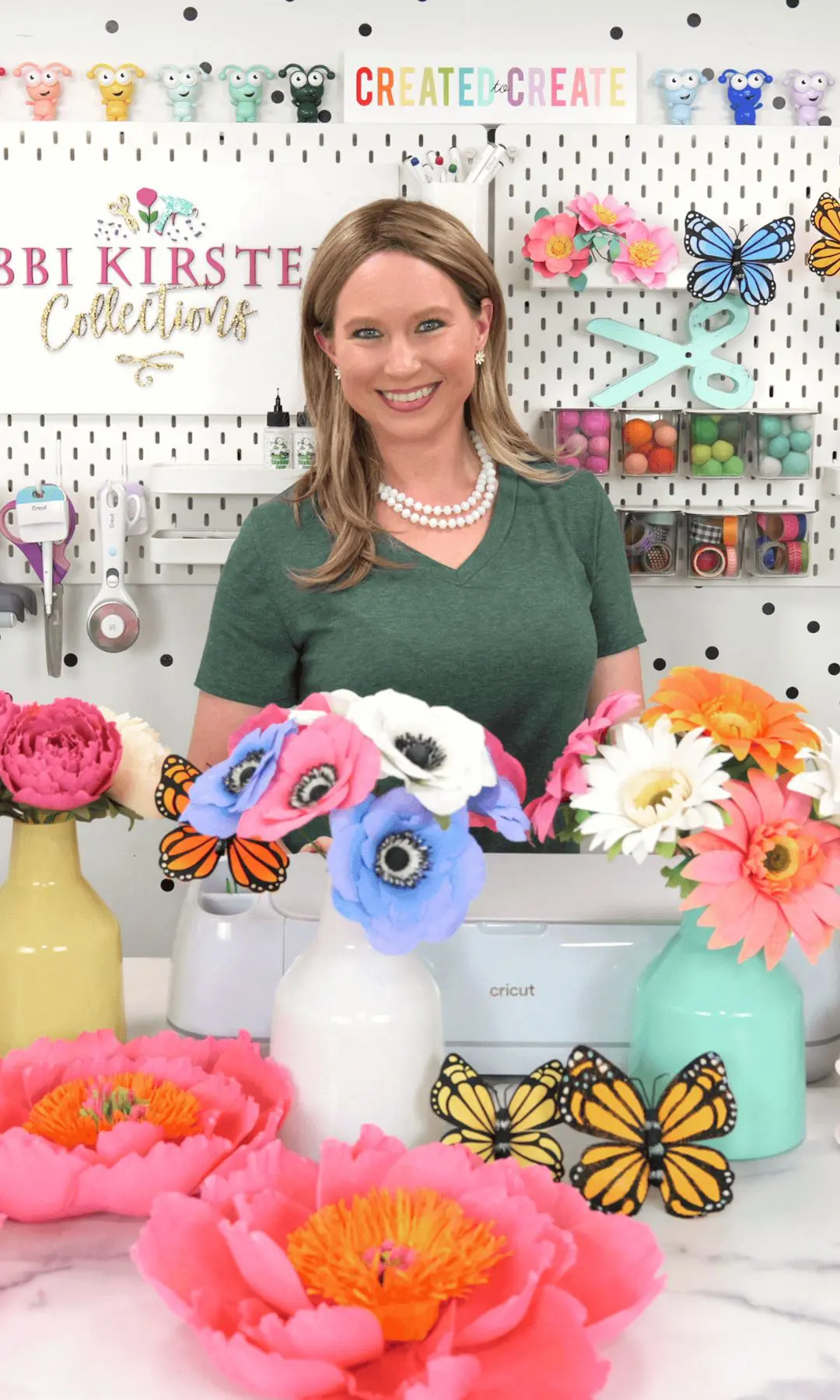 Abbi Kirsten smiling in front of a desk full of handmade crepe paper flowers