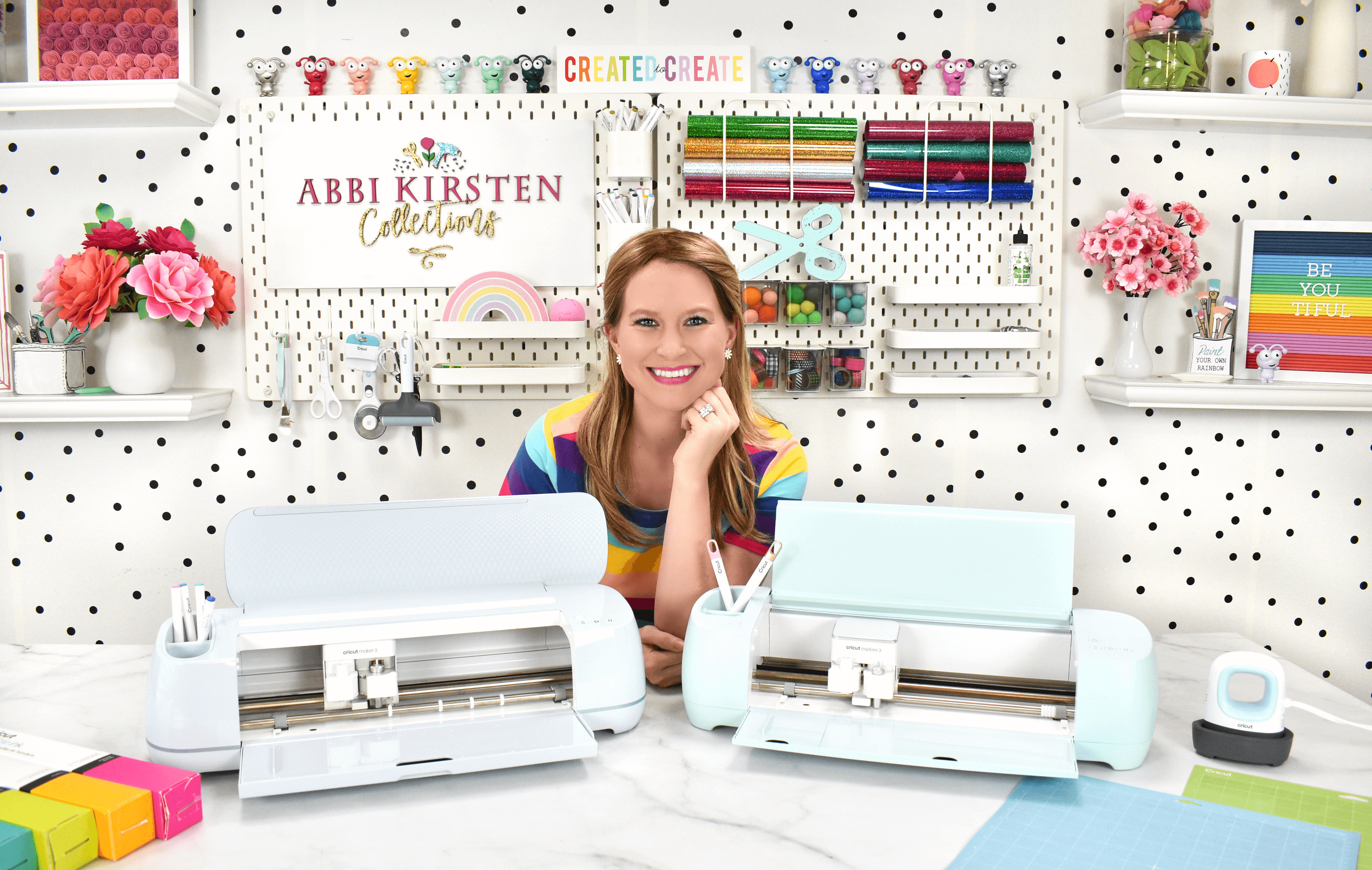 Abbi Kirsten smiling next to a Cricut Maker and Cricut Explore machine.