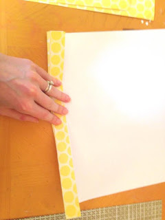 Abbi's hand shows how to make the first fold in a piece of scrapbooking paper. 