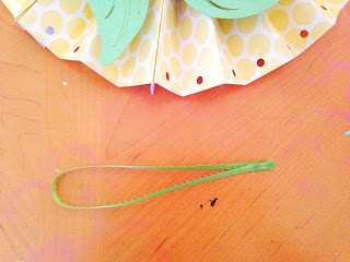 A loop of light-green ribbon lays next to the bottom of the paper rosette fan.