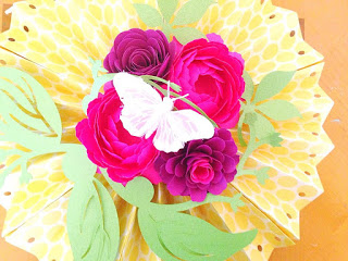 Paper fan rosettes made from scrapbooking paper with paper flowers and white butterfly on top. 