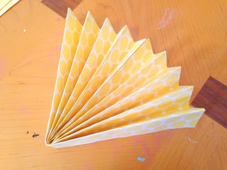 A bird's eye view of yellow and white scrapbooking paper accordion folded in half and each side attached to create a fan. 