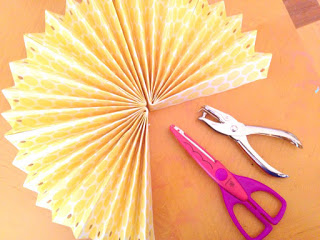 All the folded paper fan pieces are glued together. A decorative-edge scissors and a single hole punch lay next to the fan. 