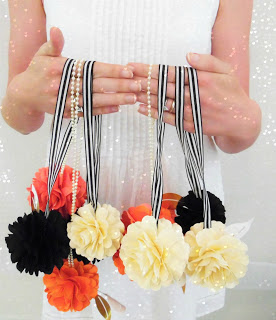 Abbi Kirsten holds black and white striped ribbon dripping with fluffy paper flowers across her chest. 