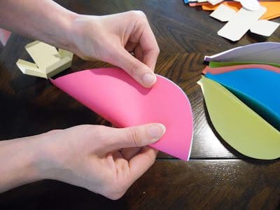 Two hands are pictured folding a pink piece of cardstock paper that has been cut into a circle.