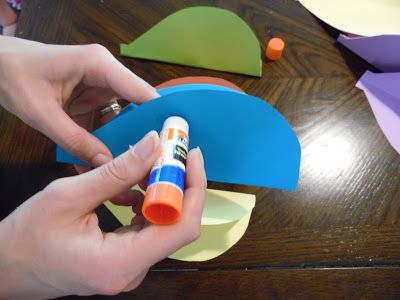 Abbi uses a glue stick to apply glue to a folded piece of blue paper to make paper hot air balloon crafts