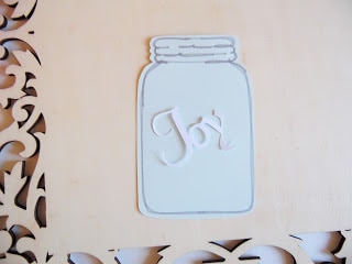 The word "Joy" has been glued to a cut-out of a blue mason jar on a wooden frame. 