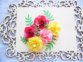 Bight paper flowers with vine leaves are glued o a decorative wooden frame as part of the wall art decor DIY process. 
