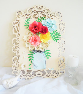 A decorative wooden frame makes fancy wall art after adding papercraft flowers and a paper mason jar as an illusion of a real vase if flowers. 