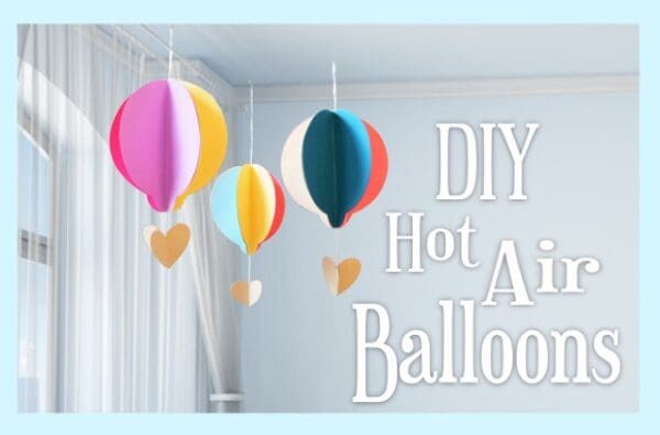 Three colorful DIY paper hot air balloons hang from a ceiling in front of a window in a bright, white room. Image text overlay reads "DIY hot hair balloons"