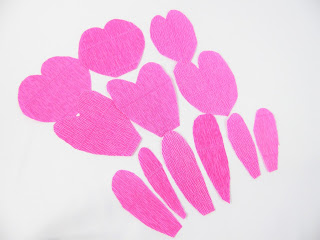 Pink crepe paper rose petals and piece lay on a white background ready to be made into a gorgeous crepe paper flower. 