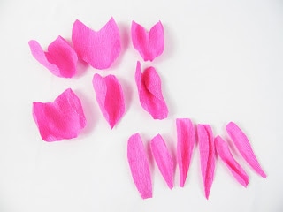 Crepe paper rose petals sit on the white paper background, slightly curled inward to mimic the shape of a natural rose. 