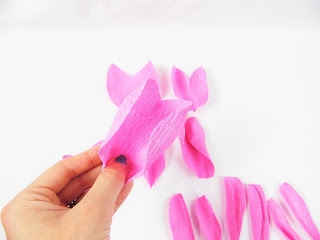 Abbi Kirsten's hand holds a curled crepe paper rose petal in her hand. The remaining curled crepe paper petals lay in the background. 