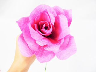 In Abbi Kirsten's hand is a crepe paper flower with some larger petals added, showing how full the final paper flower will become. 