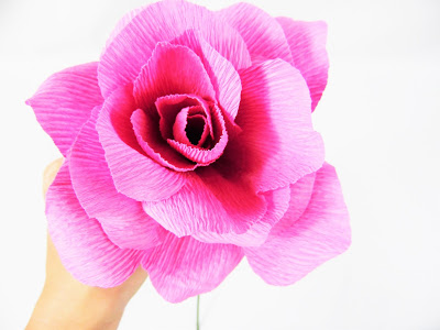 A woman holds a bright pink paper rose in her hands made with tissue paper rose petals.