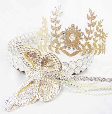 A gold and diamond-looking butterfly headpiece complete with a crown lays on a white background. 