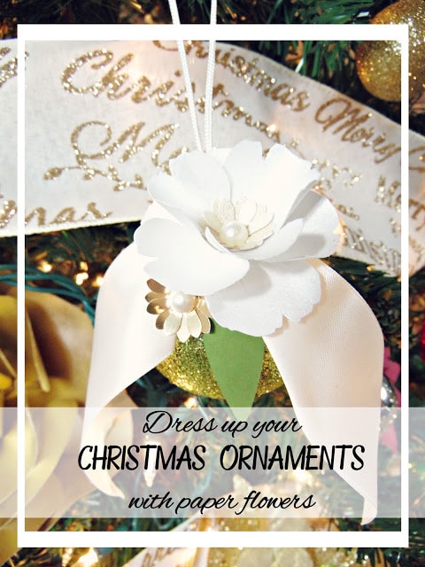 A graphic of an ornament covered with white ribbons and white paper flowers, surrounded by gold lettering and gold flowers. The text reads, "Dress up your Christmas ornaments with paper flowers."