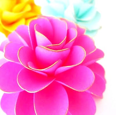 A closeup image of a pink ruffle Dahlia paper flower with thin yellow edges around the paper petals.