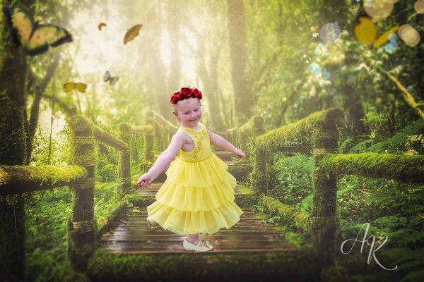 A little girl in a yellow dress and red paper poppy crown dancing on a moss-covered wooden bridge. There are yellow butterflies flying nearby. 