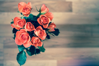 A bird's eye view of a bouquet of orange flowers blooming over their green leaves. An out of focus wooden table top is below. Baby shower favors are great crafts. 