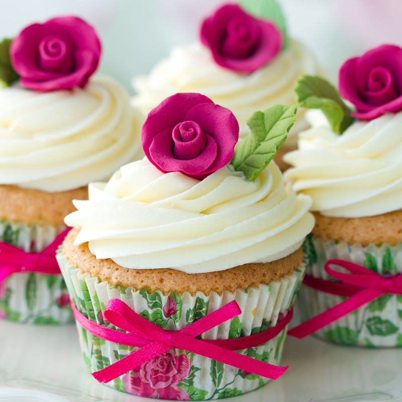 Vanilla iced cupcakes wrapped with thin pink ribbon and topped with a pink fondant rosette.