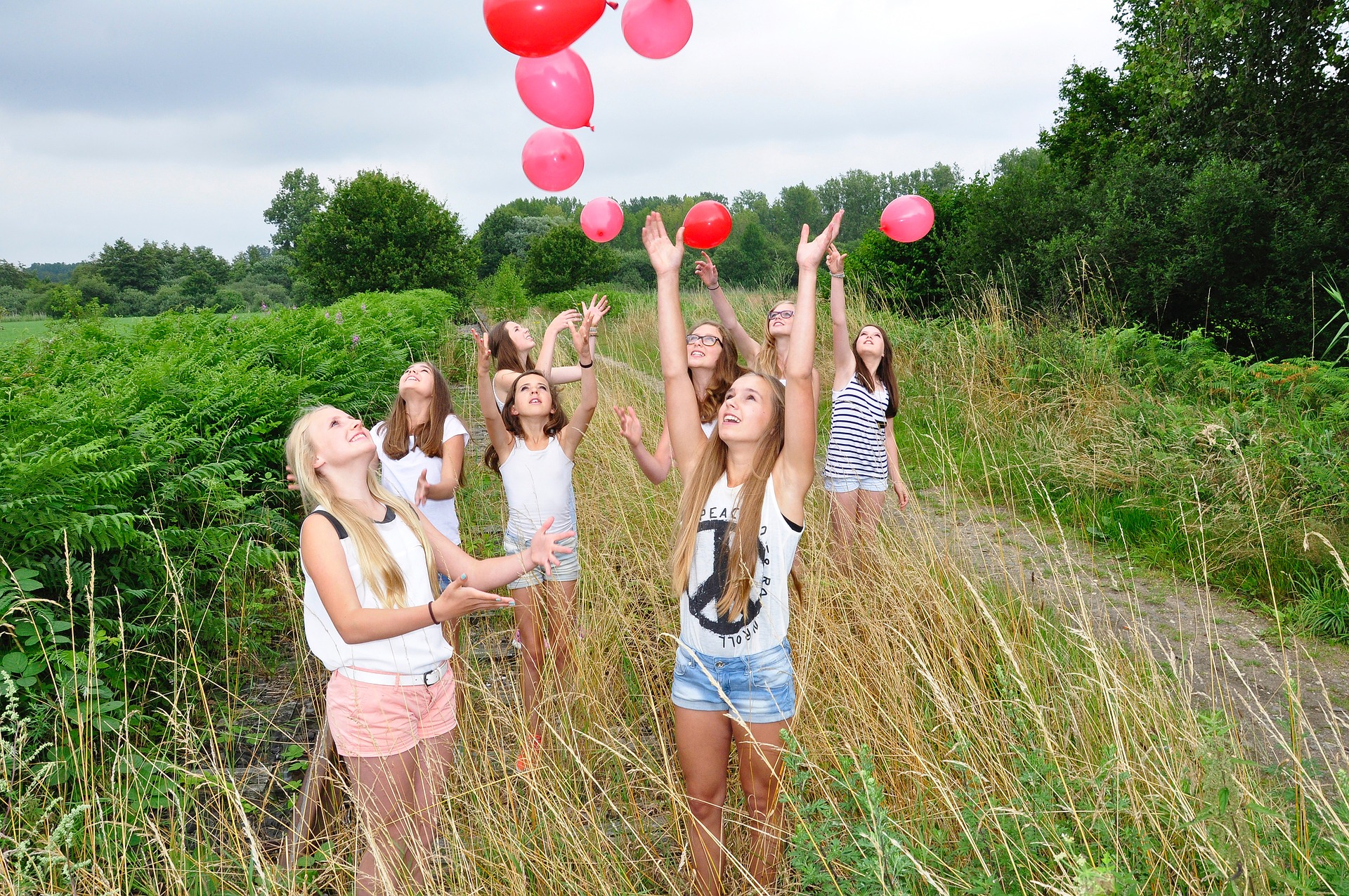 A group of teenage girls stand in a grassy field, releasing ink balloons into the air.