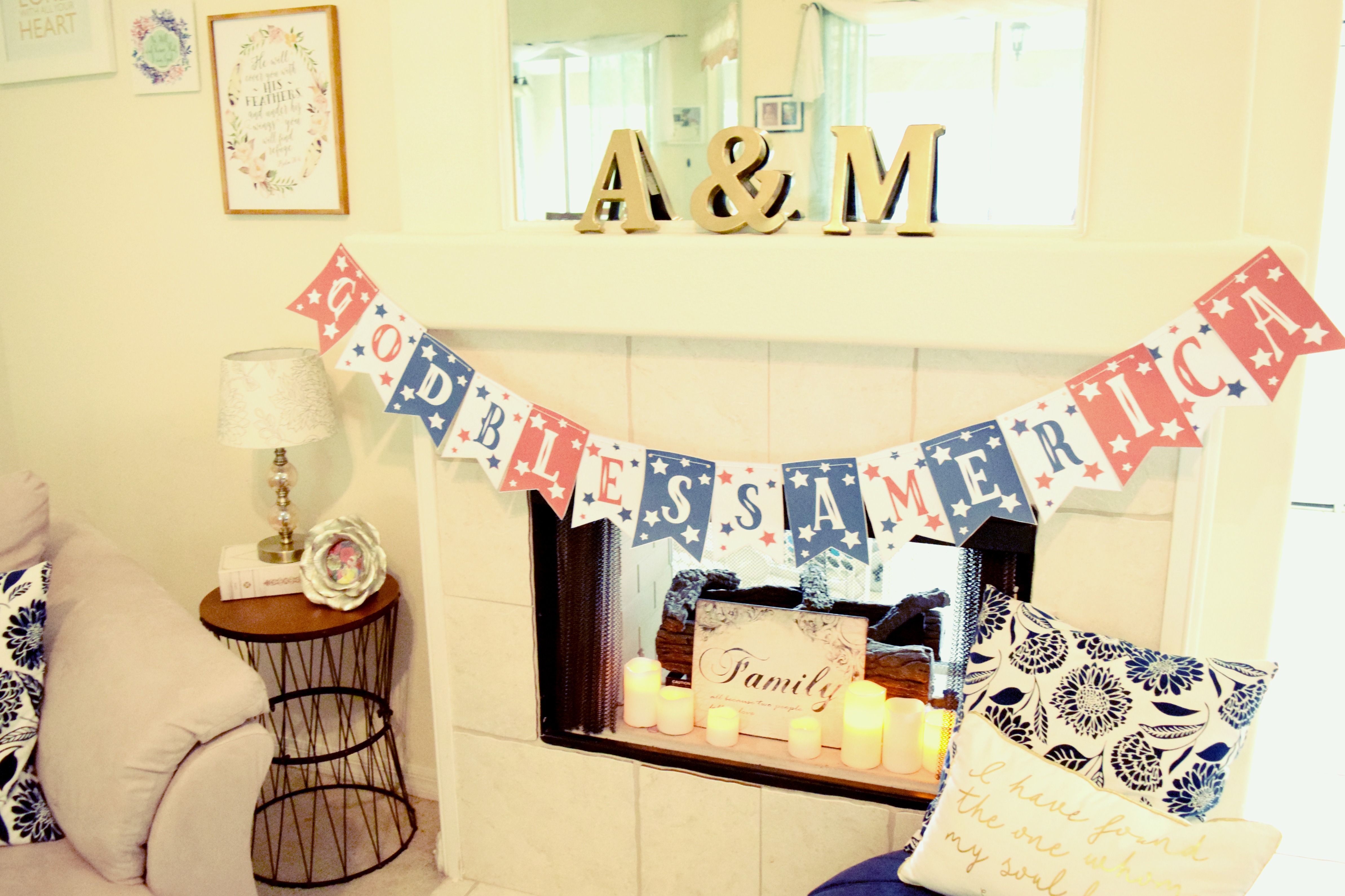 A red, white, and blue GOD BLESS AMERICA banner hangs across a white fireplace mantel in a living room.