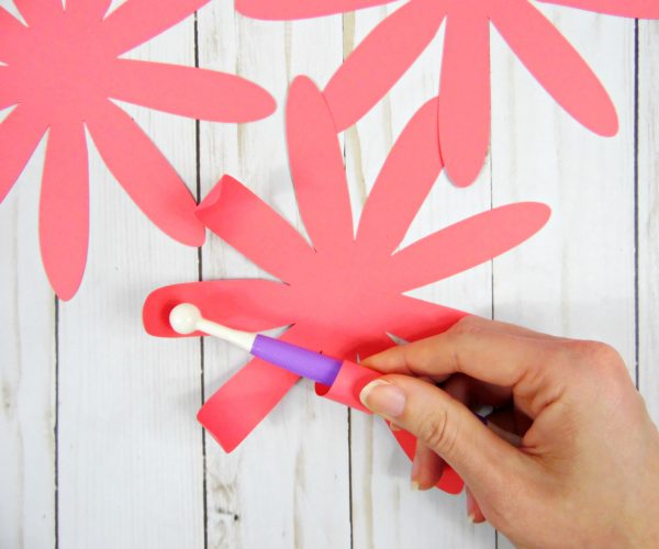 Abbi uses a Cricut rolling tool to roll the edges of a pink paper Chrysanthemum Flower layer, making the very edge of the flower petals roll upwards in a natural way.