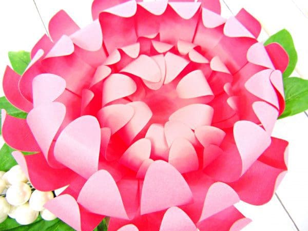 A completed pink paper Chrysanthemum Flower with seven layers of curled petals, and faux green leaves around the outside of the flower.