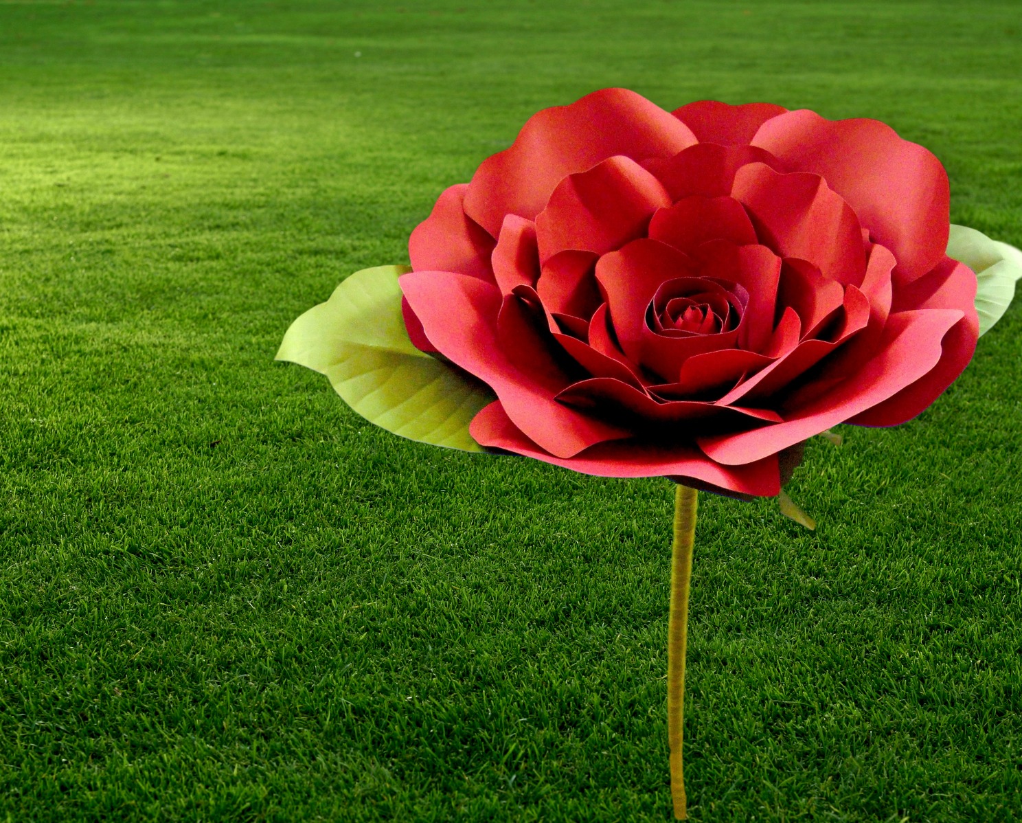 A giant paper red rose stands in a green manicured lawn. In this giant paper flower stem tutorial, you can make your own large flower stems from wood dowels.