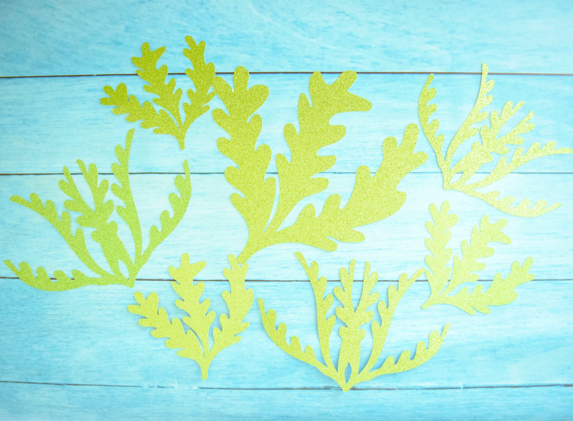 Glitter paper cutouts of seaweed shapes rest on a blue background.