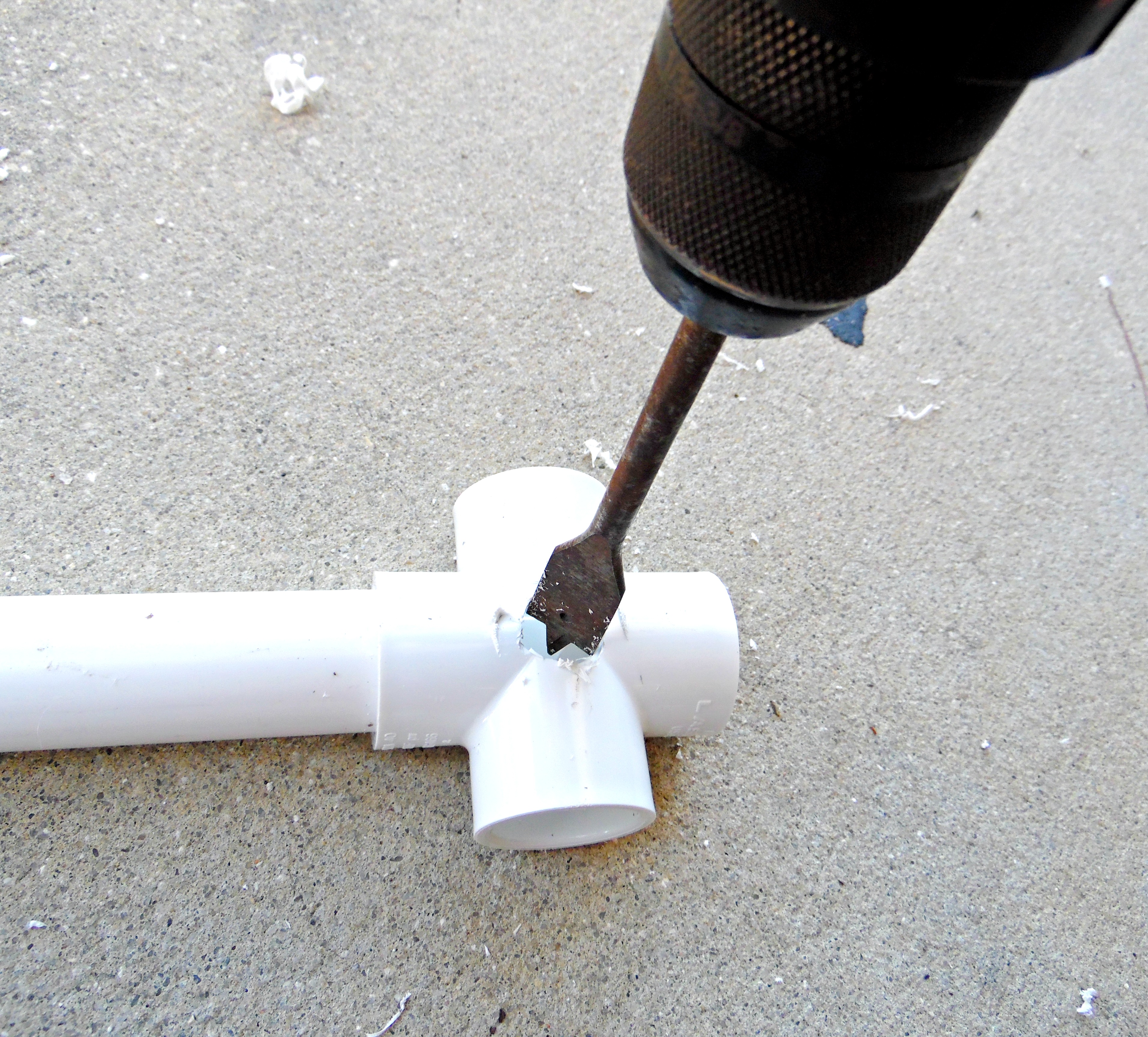 Using a larger drill spade to create a larger hole in the PVC 4-way base for the giant paper flower stand. 