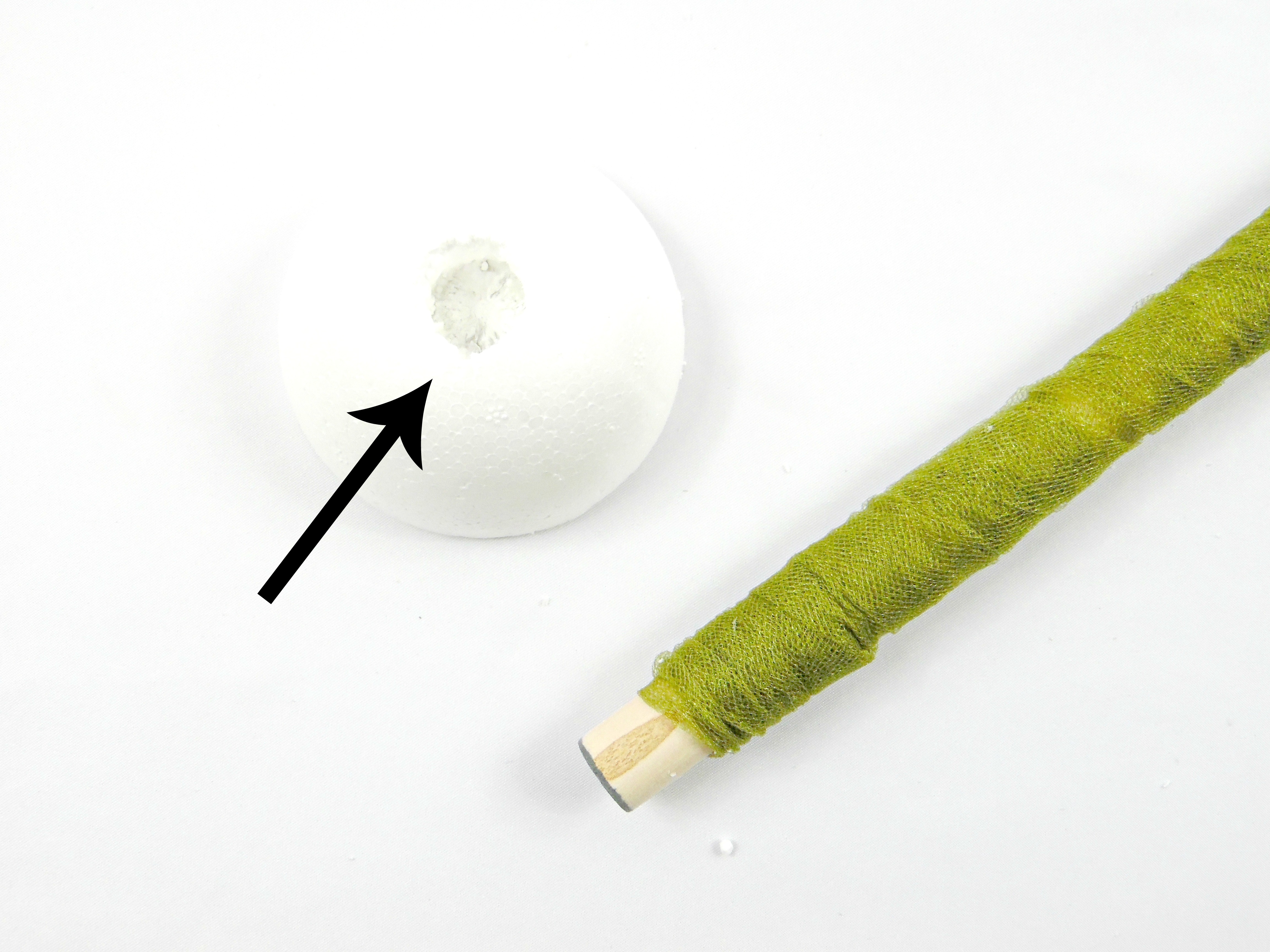 A foam ball, cut in half, has a deep dowel-sized hole in its center. Using the wooden dowel to carve out this hole is step 3 in the giant paper flower stem tutorial. 