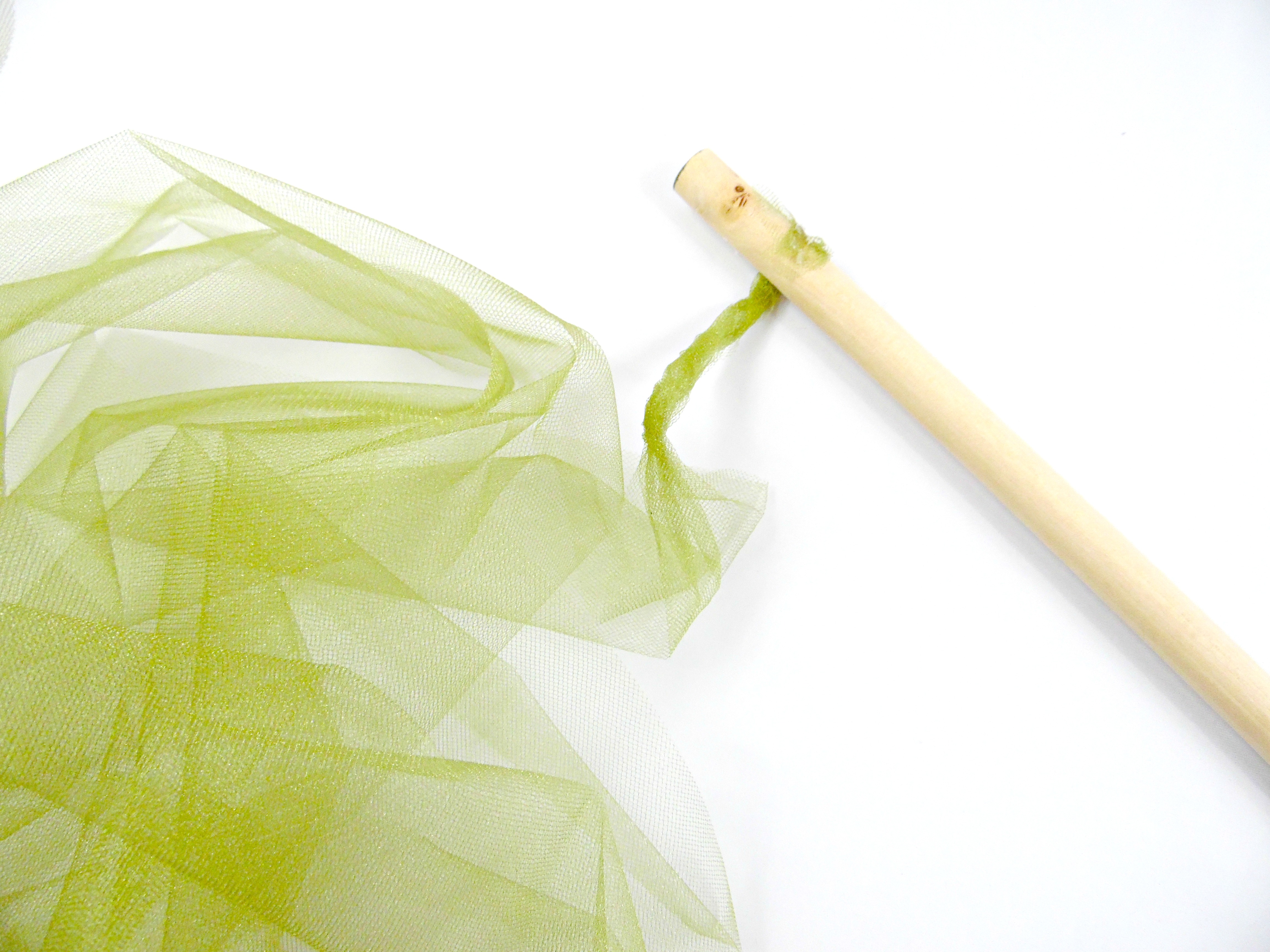 Start wrapping the wooden dowel rod with the green tulle fabric about an inch from the end of the dowel. The tulle is glued in place and twisted to create a whimsical, textured flower stem.