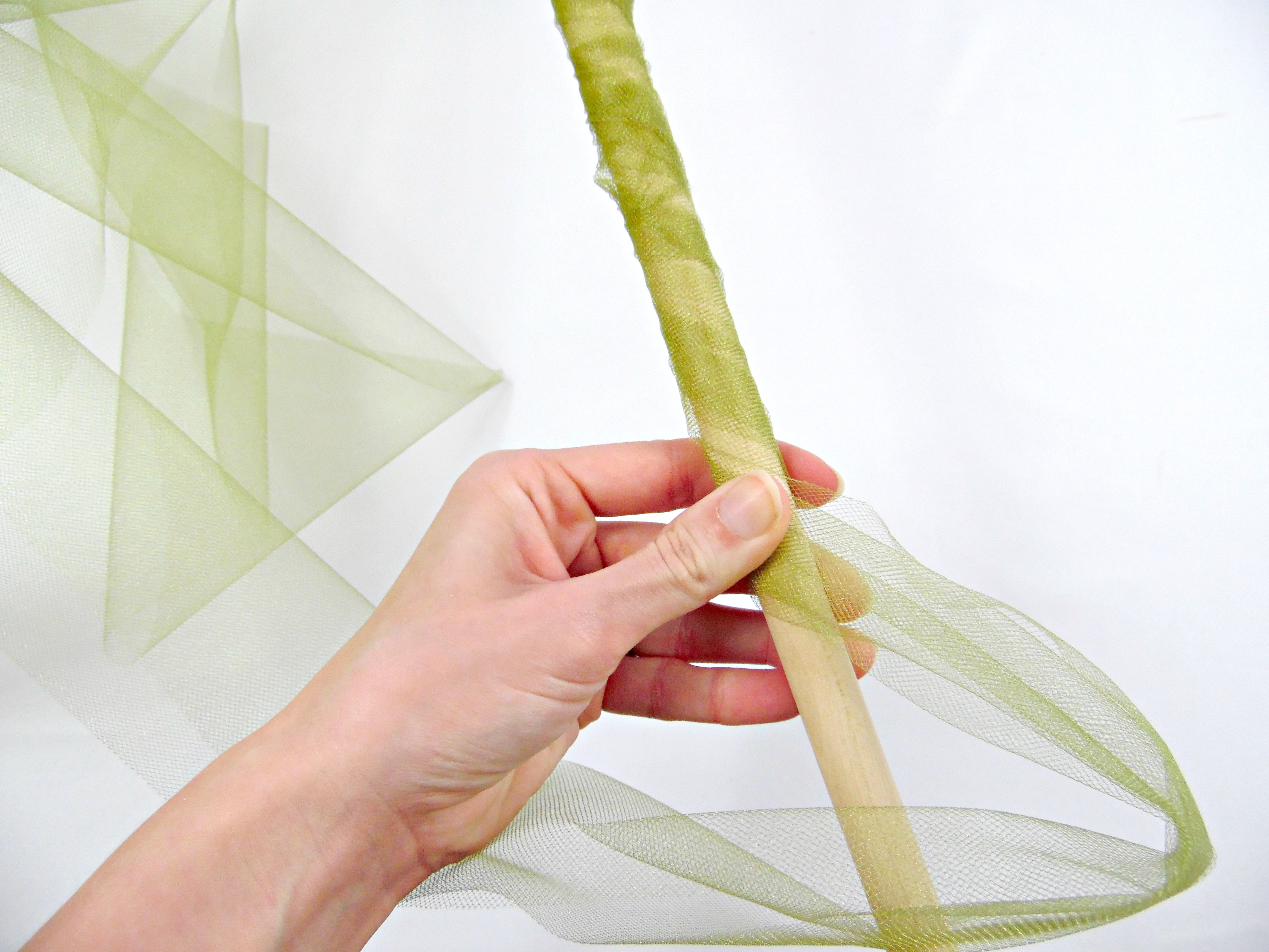 The process of wrapping green tulle fabric around a wooden dowel to create a giant paper flower stem.  