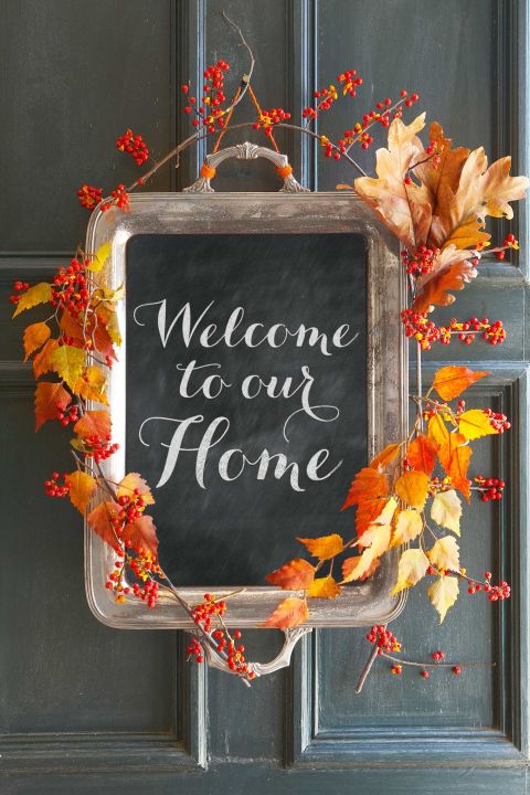 A chalkboard sign hangs on a black front door. The chalkboard says "welcome to our home" and is surrounded by branches of faux Fall leaves and berries.