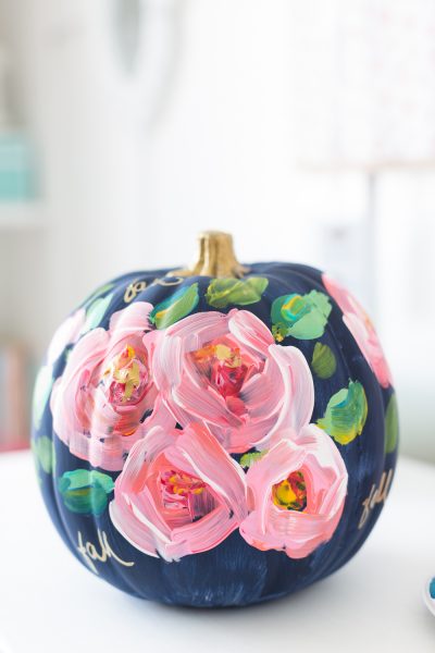 A medium sized craft pumpkin is painted navy blue with pastel pink flowers and green leaves on the front.
