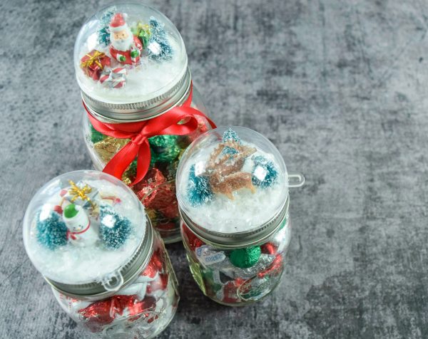 Three DIY snowglobe mason jar Christmas crafts are completed when filled with candy, bath salts, or other gifts. 